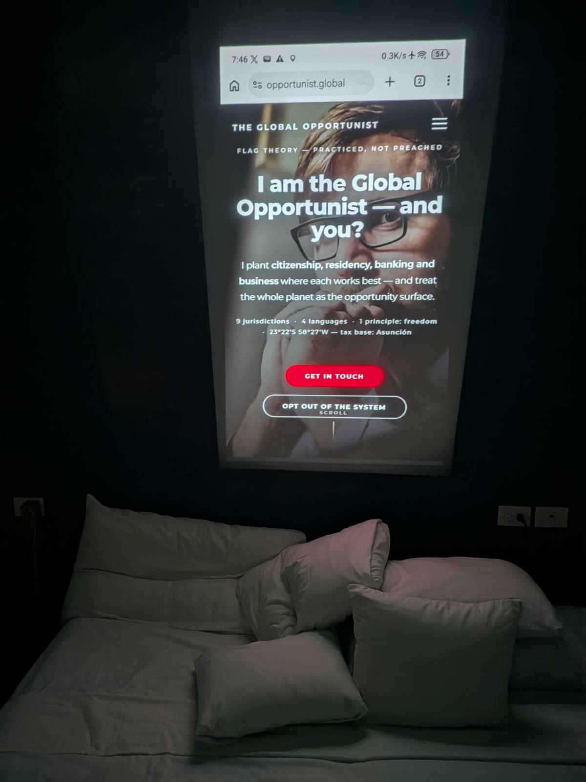 Tank 5 Pro projecting the opportunist.global website onto a dark wall above a bed